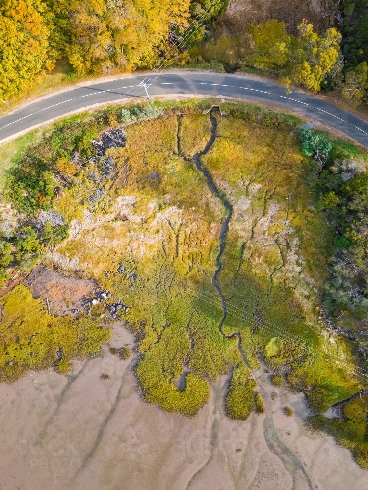 Aerial view of a small creek winding through marshland and under a curve in the road. - Australian Stock Image