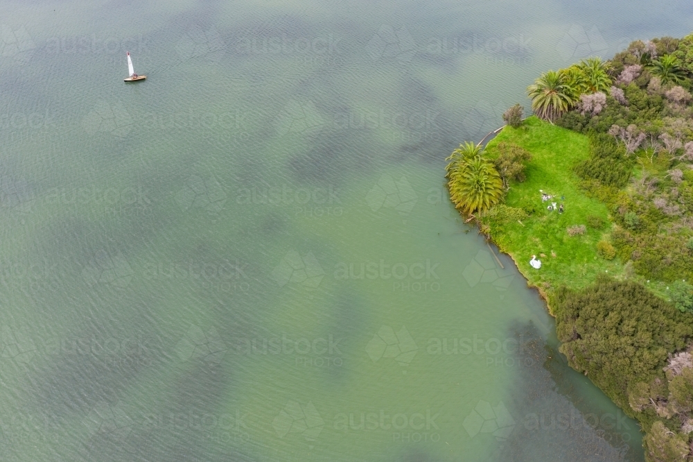 Aerial view of a small yacht floating on a lake near people relaxing on an island - Australian Stock Image