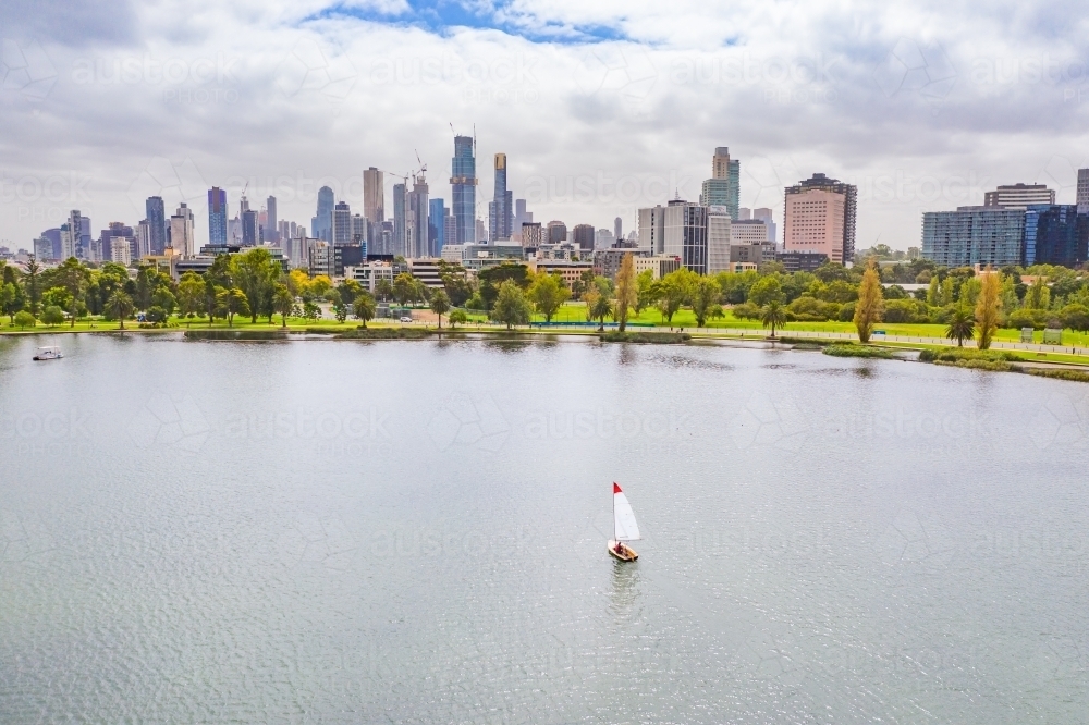 Aerial view of a small yacht on a lake in front of a city skyline - Australian Stock Image