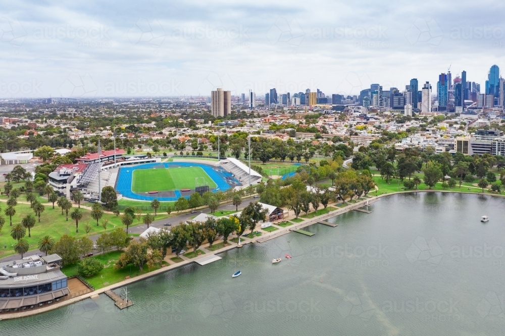 Aerial view of a sporting arena on the shores of a lake in front of a city skyline - Australian Stock Image