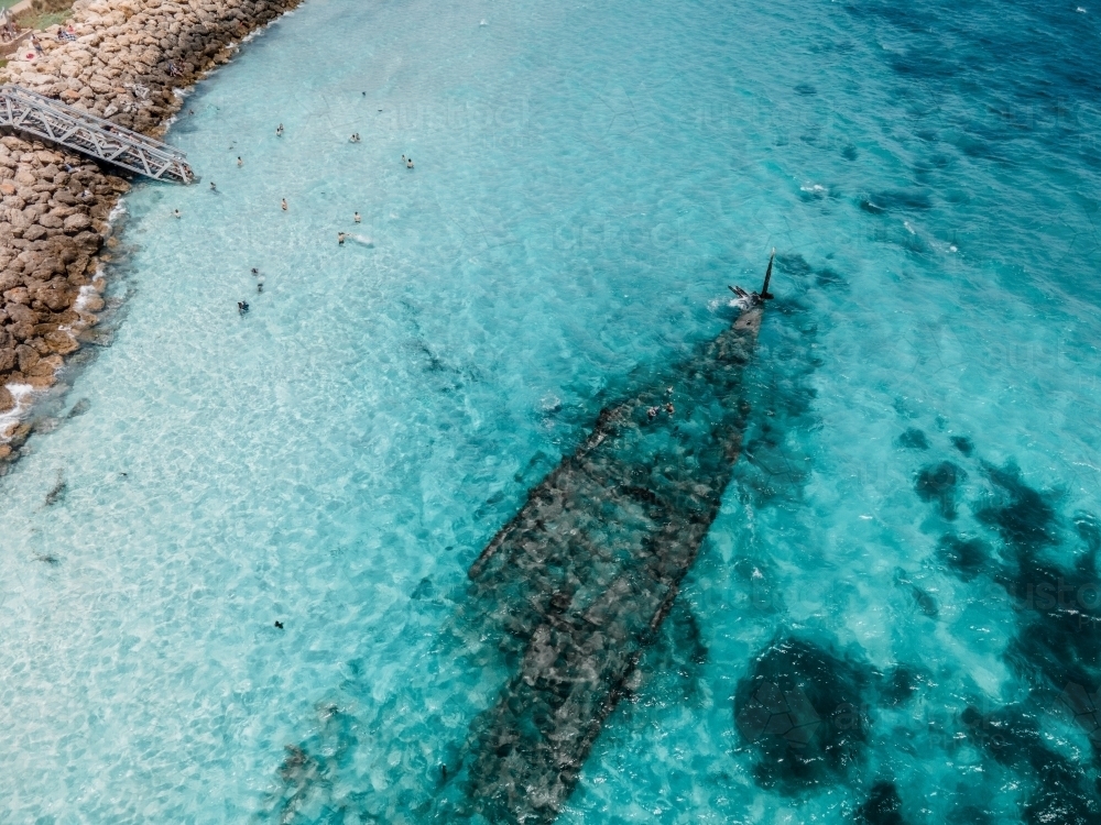 Aerial view of a sunken ship with people swimming, white sand, bushes and grass - Australian Stock Image