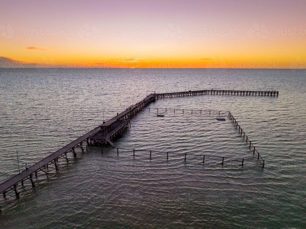Aerial view of a sunset glow over a coastal jetty with a swimming enclosure - Australian Stock Image