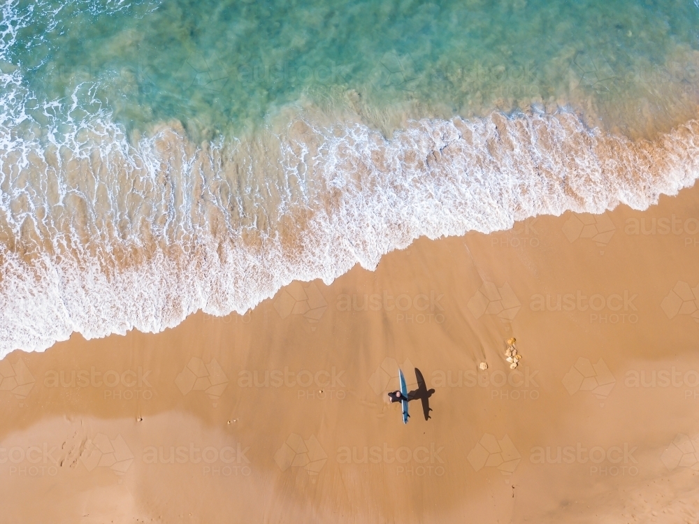 Image of Aerial view of a surfer walking down a beach towards the waves ...
