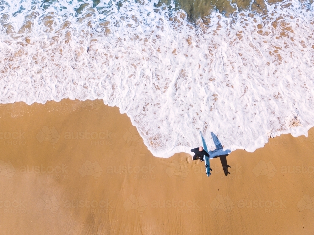 Aerial view of a surfer walking down a beach towards the waves - Australian Stock Image