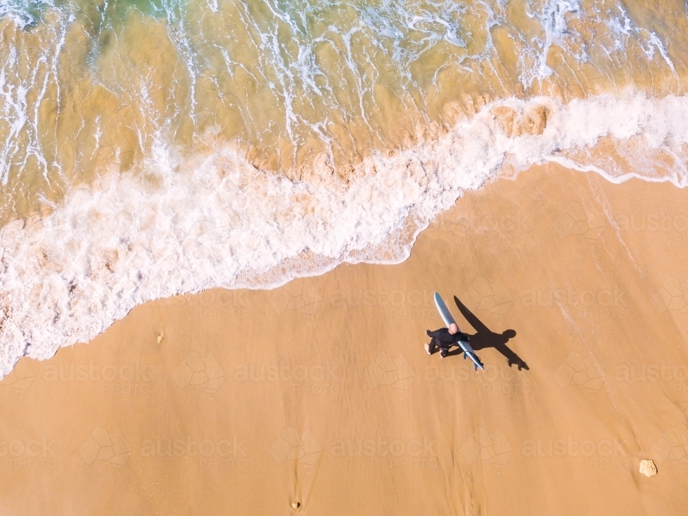 Image of Aerial view of a surfer walking down a beach towards the waves ...
