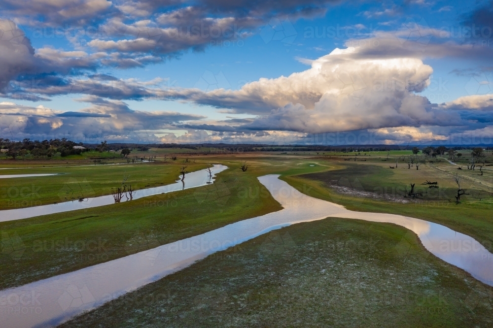Aerial view of a system of narrow rivers winding into the distance under a dramatic cloudy sky - Australian Stock Image