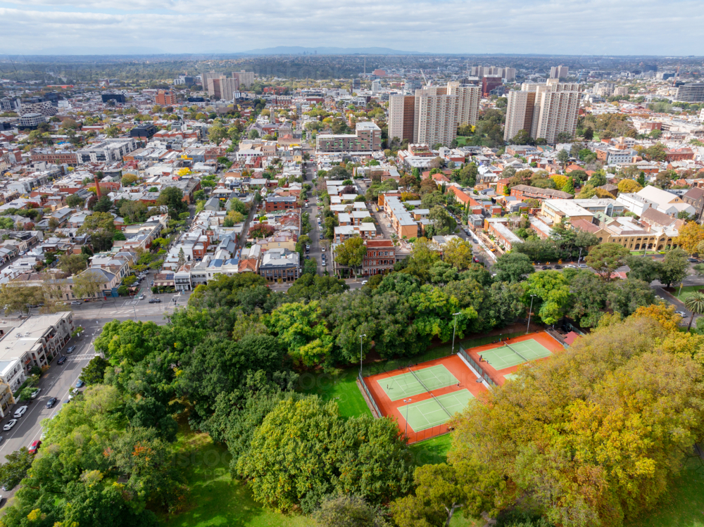 Aerial view of a tennis court in an inner city park surrounded by trees and low rise buildings - Australian Stock Image