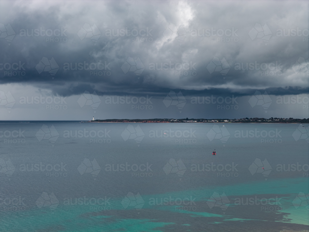 Aerial view of a tiny boat on a calm bay under rain falling from a dark stormy sky - Australian Stock Image