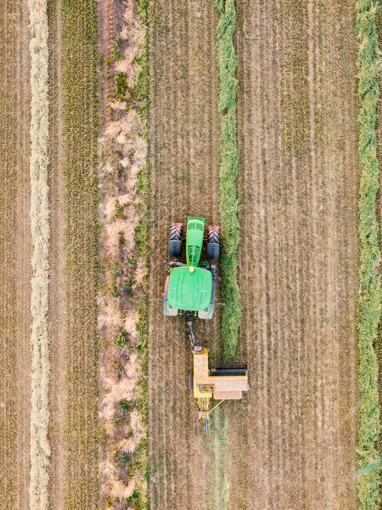 Aerial view of a tractor collecting rows of feed in a paddock - Australian Stock Image