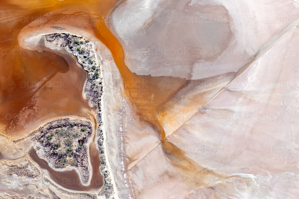 Aerial view of a vivid orange and pink salt lake shoreline with a small vegetated island - Australian Stock Image