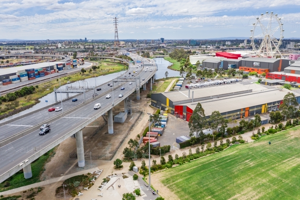 Aerial view of a wide freeway overpass with a sporting field below and ferris wheel in the distance - Australian Stock Image