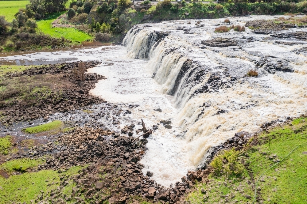 Aerial view of a wide rocky waterfall tumbling into a green valley - Australian Stock Image