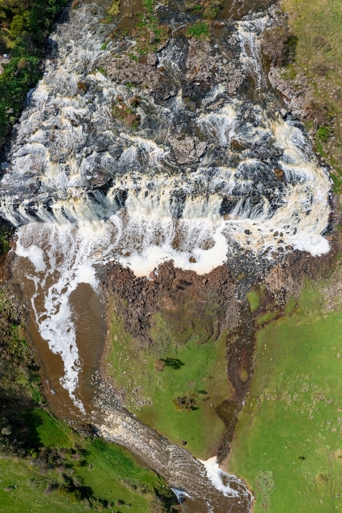 Aerial view of a wide rocky waterfall tumbling into a green valley - Australian Stock Image
