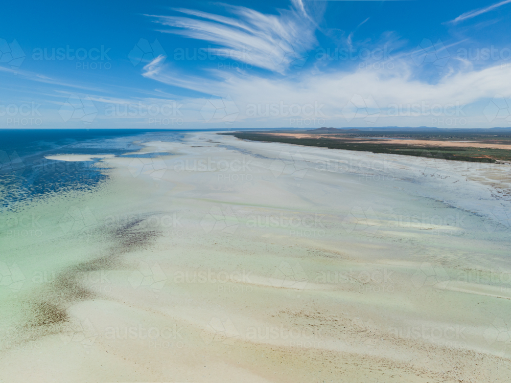 Aerial view of a wide white sand beach at low tide with blue sky above - Australian Stock Image