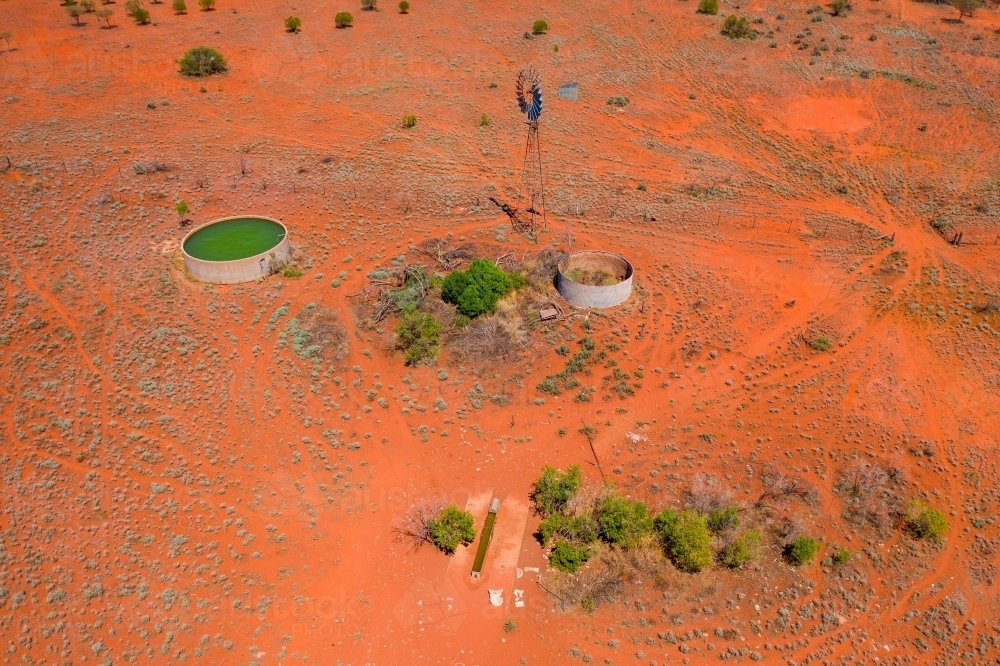Aerial view of a windmill and drinking trough on red barren land - Australian Stock Image