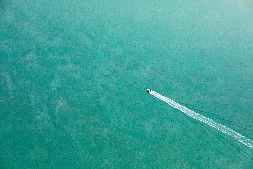 aerial view of boat heading out in blue green sea - Australian Stock Image