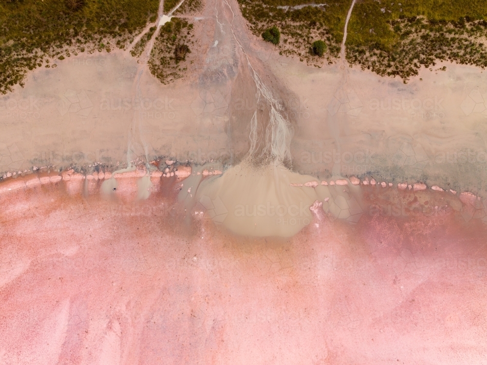 Aerial view of brown silt draining on to a pink salt lake - Australian Stock Image
