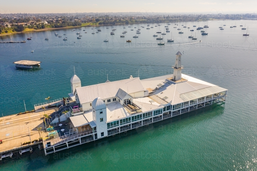 Aerial view of buildings on the end of a pier over a bay with boats anchored in the background - Australian Stock Image