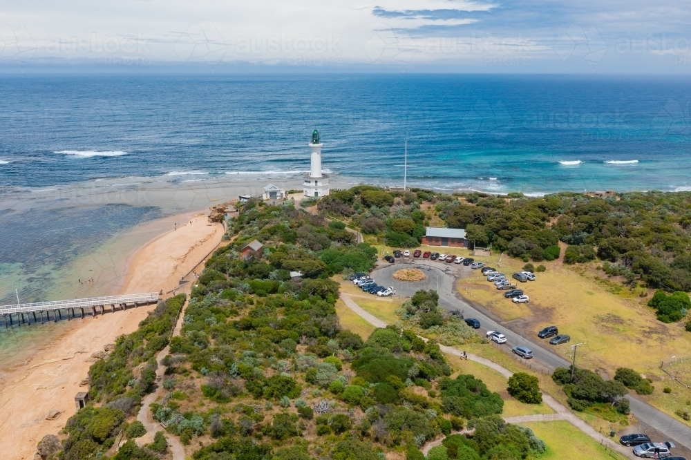 Aerial view of car park and pier near the base of a lighthouse on a coastal cliff - Australian Stock Image