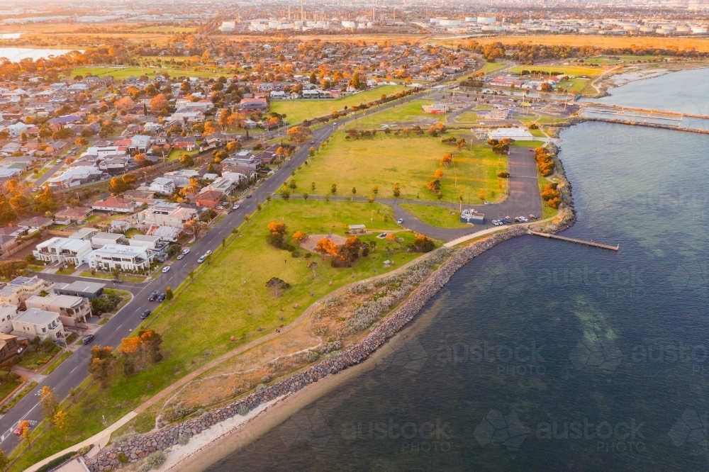 Aerial view of coastal reserve and suburb next to a calm bay at sunset - Australian Stock Image