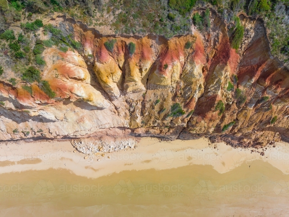 Aerial view of colourful eroded cliffs with rocks scattered on the beach below - Australian Stock Image