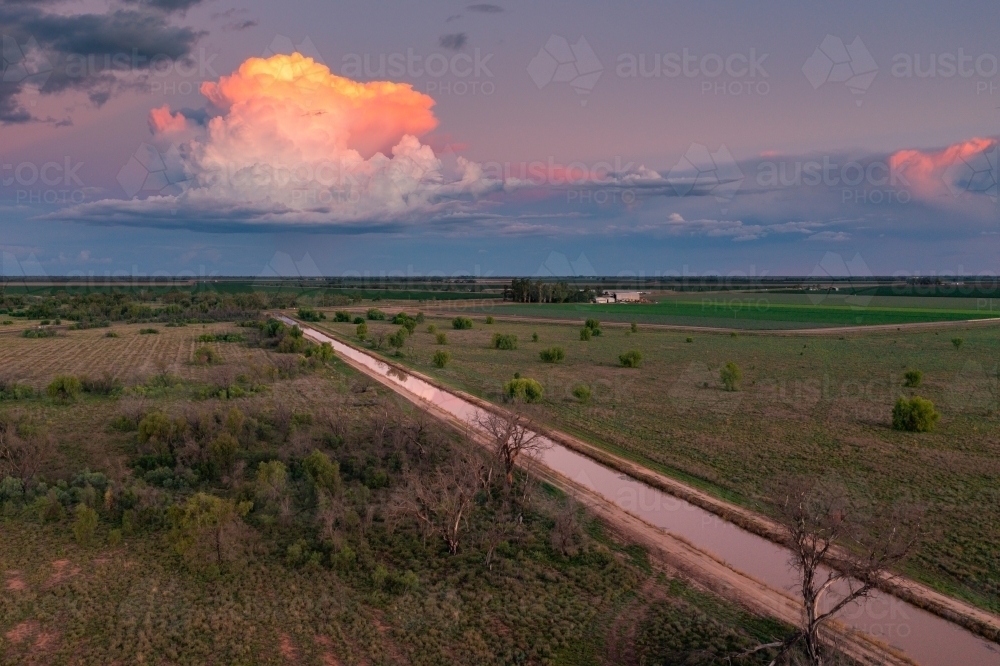 Aerial view of colourful storm clouds at twilight over an irrigation channel on farmland - Australian Stock Image