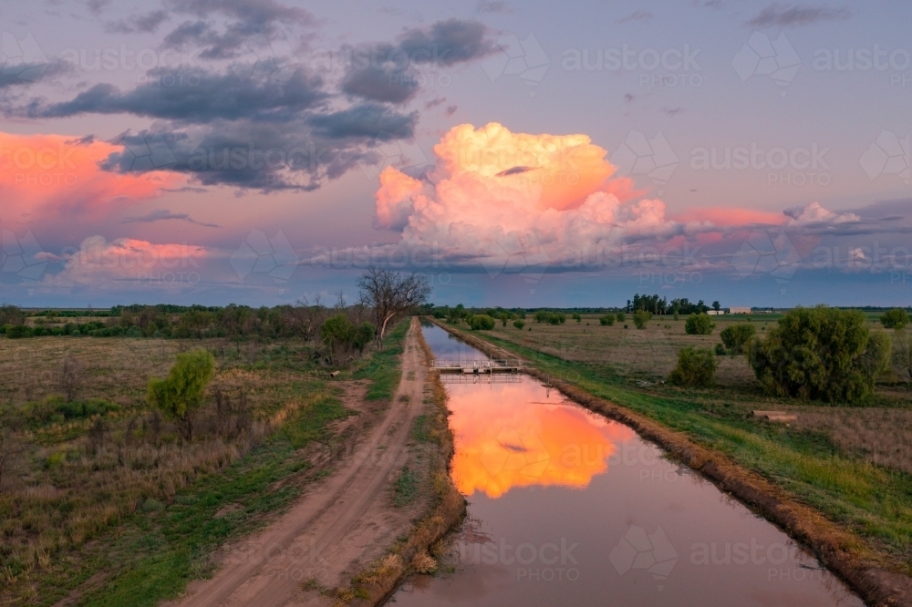 Aerial view of colourful storm clouds at twilight reflected in the water of an irrigation channel - Australian Stock Image