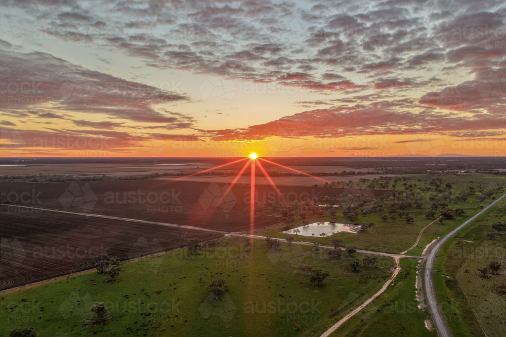 Aerial view of cultivated fields surrounded by a lush green landscape as the rising sun climbs above - Australian Stock Image