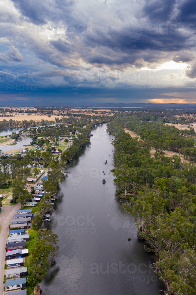Aerial view of dark storm clouds gathering over a tourist park on the banks of an inland river - Australian Stock Image