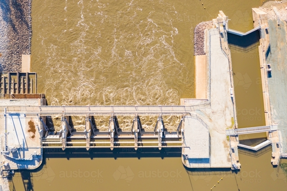 Aerial view of dirty river water rushing through the gates of a weir - Australian Stock Image