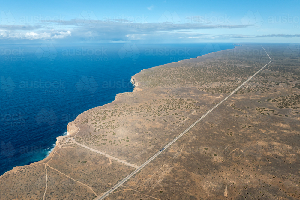 Aerial view of dramatic limestone cliffs dropping to deep blue ocean beside a straight outback road - Australian Stock Image