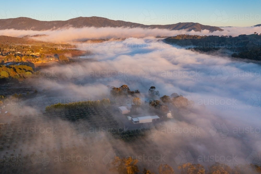Aerial view of early morning light over a layer of fog covering rural farmland - Australian Stock Image