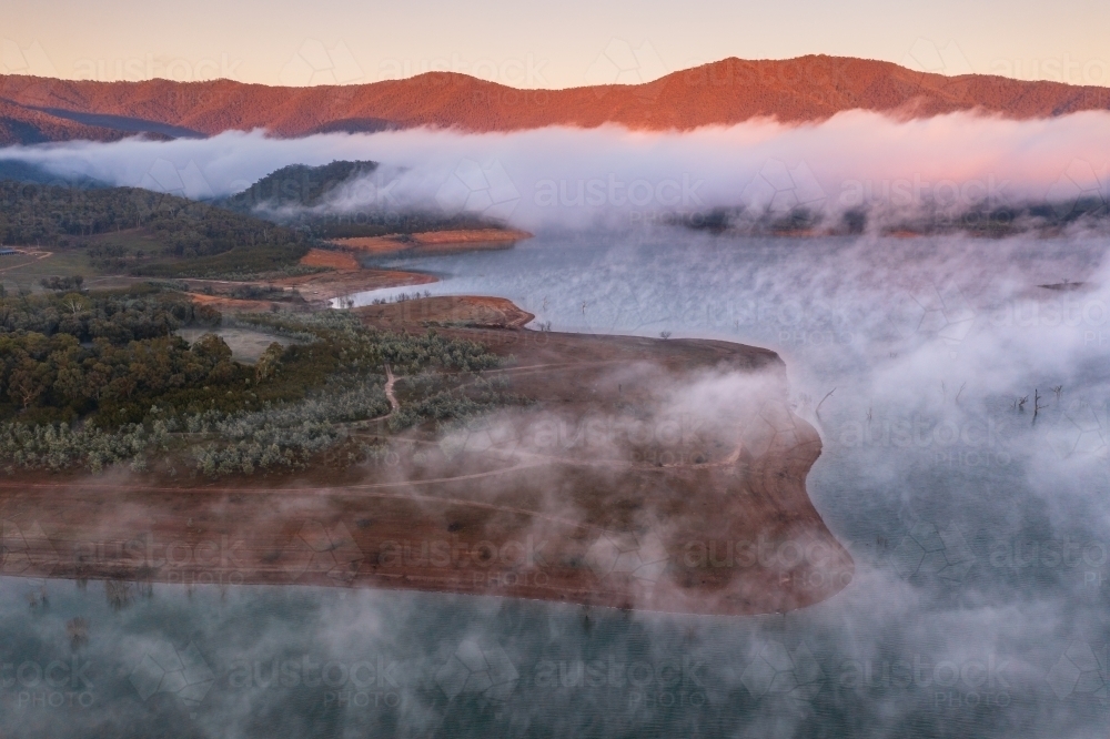 Aerial view of early morning light over a mountain lake covered with fog - Australian Stock Image