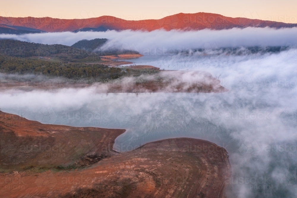 Aerial view of early morning light over a mountain lake covered with fog - Australian Stock Image
