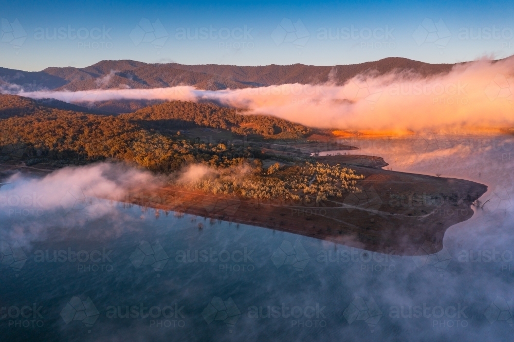 Aerial view of early morning light over a mountain lake covered with fog - Australian Stock Image