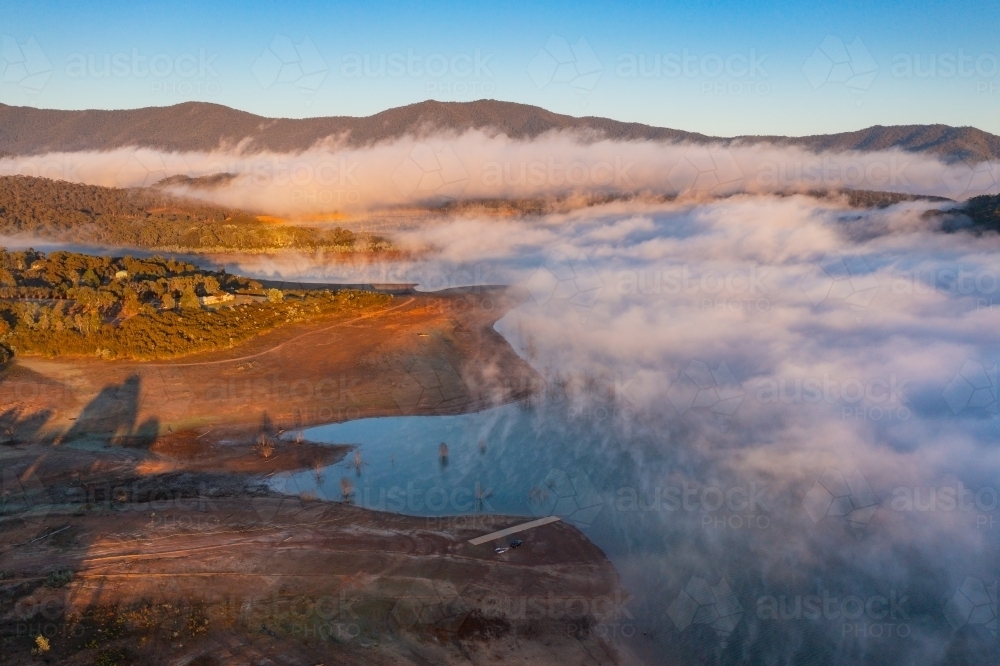 Aerial view of early morning light over a mountain lake covered with fog - Australian Stock Image