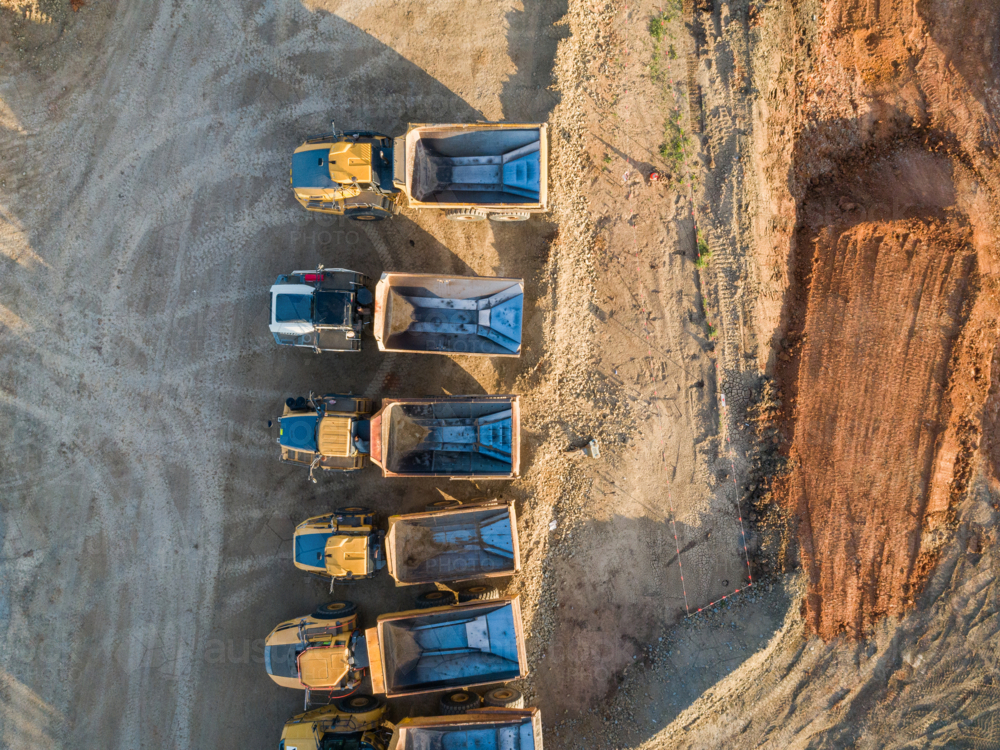 Image of Aerial view of empty dump trucks lined up on worksite in ...