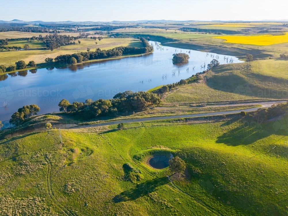 Aerial view of farmland and a country road around a widening river - Australian Stock Image
