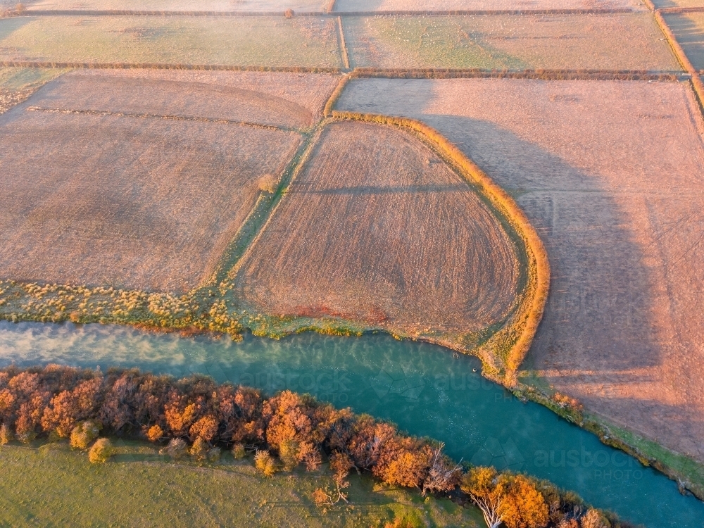 Aerial view of farmland and autumn trees on the banks of a river - Australian Stock Image