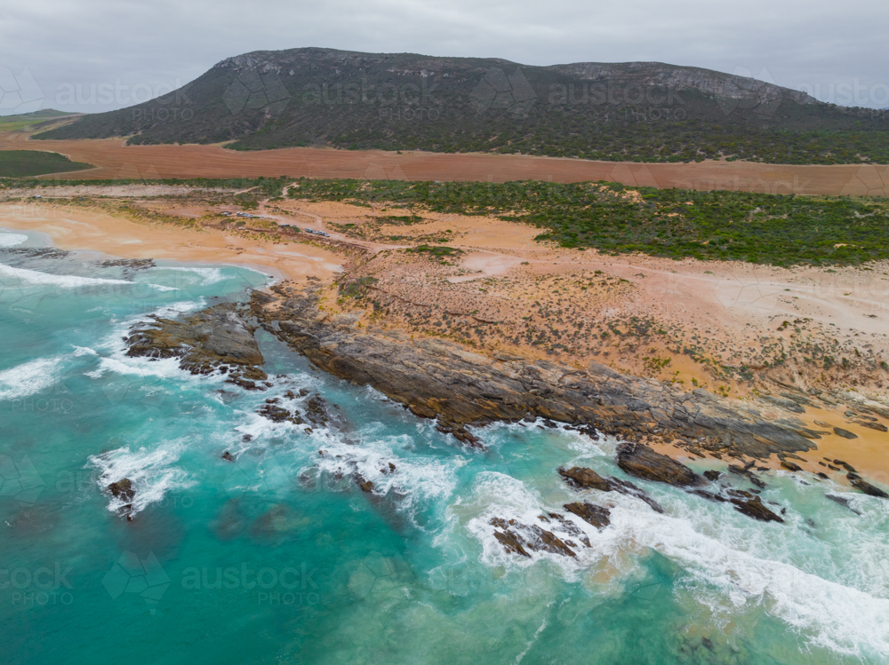 Aerial view of foamy waves breaking over rocks along a rugged uninhabited coastline - Australian Stock Image