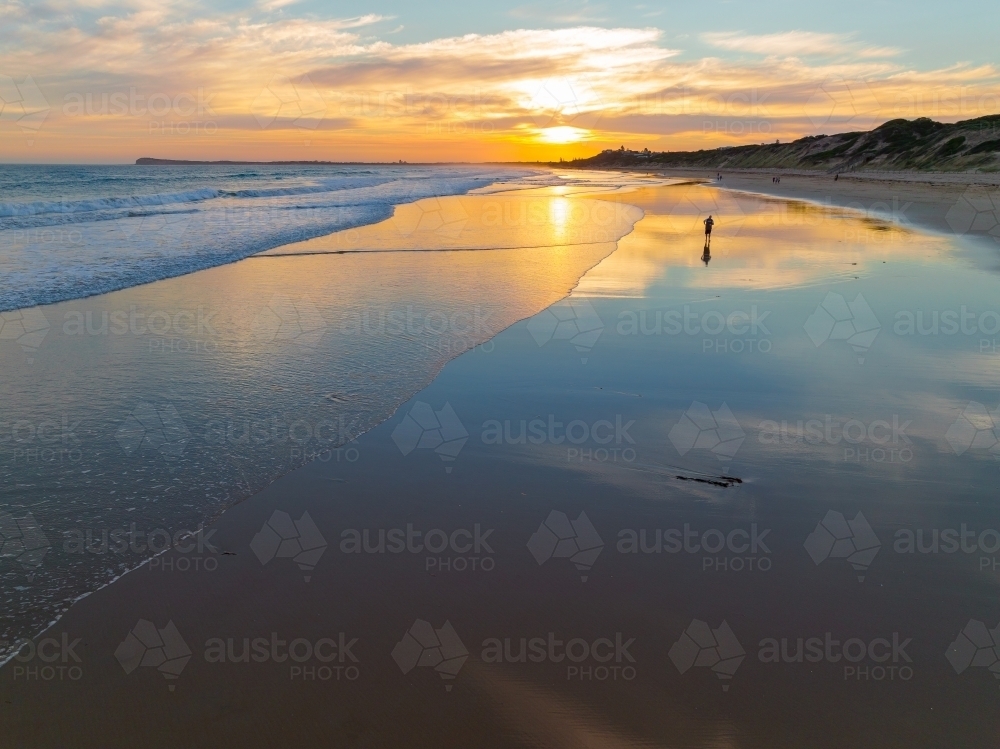 Aerial view of gentle waves on a beach with reflection of a sunset - Australian Stock Image