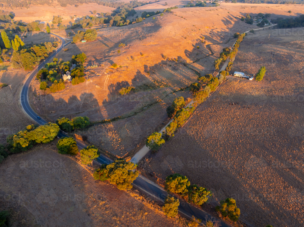 Aerial view of golden evening light on country roads running through dry rural farmland - Australian Stock Image