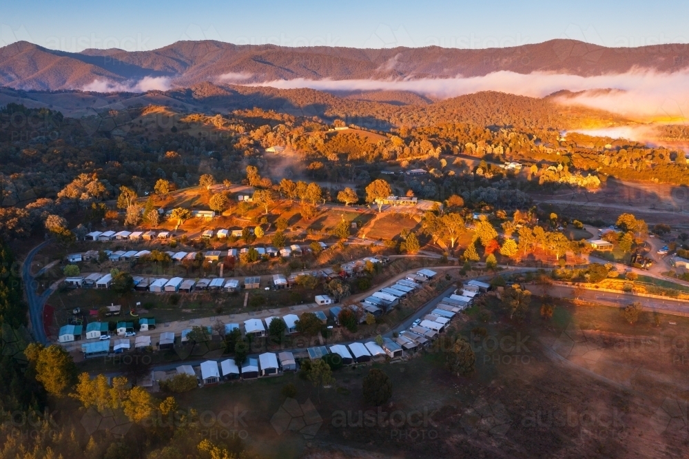 Aerial view of golden morning light on a caravan park nestled among mountains - Australian Stock Image