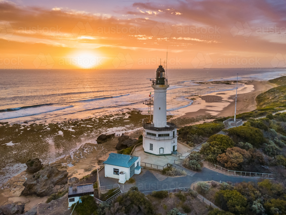 Aerial view of golden sunset over a lighthouse on a coastal cliff - Australian Stock Image