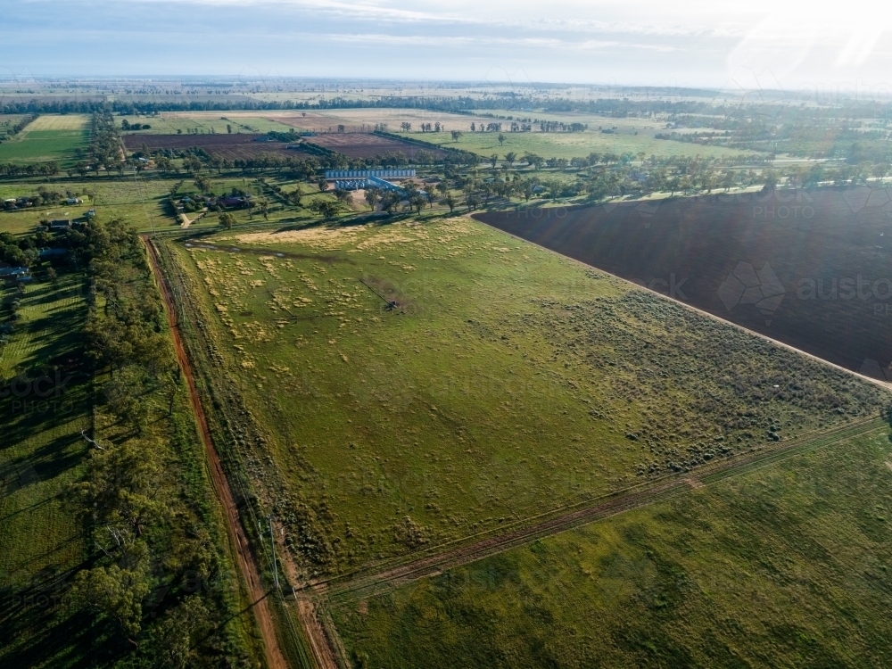 Aerial view of gravel road to Aussie farm and green grassy paddocks in morning light - Australian Stock Image