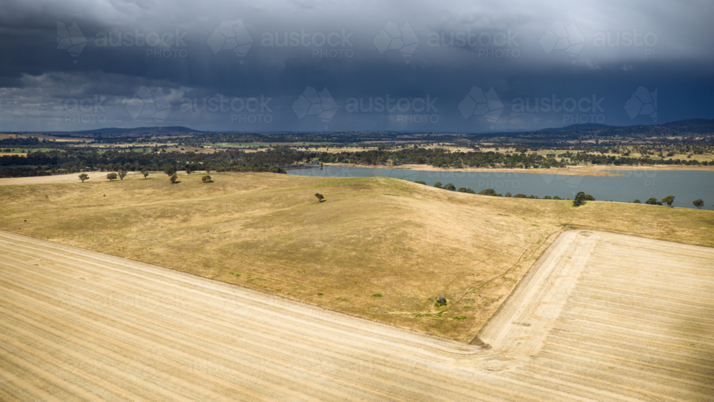 Aerial view of heavy rain falling from dark clouds advancing over an inland lake and dry farmland - Australian Stock Image
