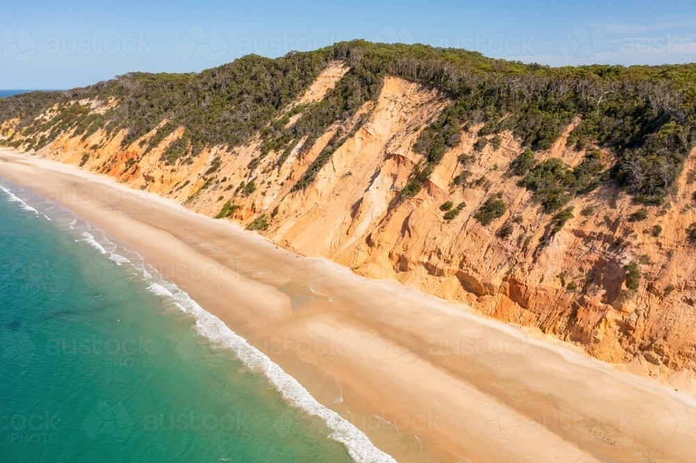 Aerial view of high colourful sea cliffs above a narrow beach and a blue ocean - Australian Stock Image