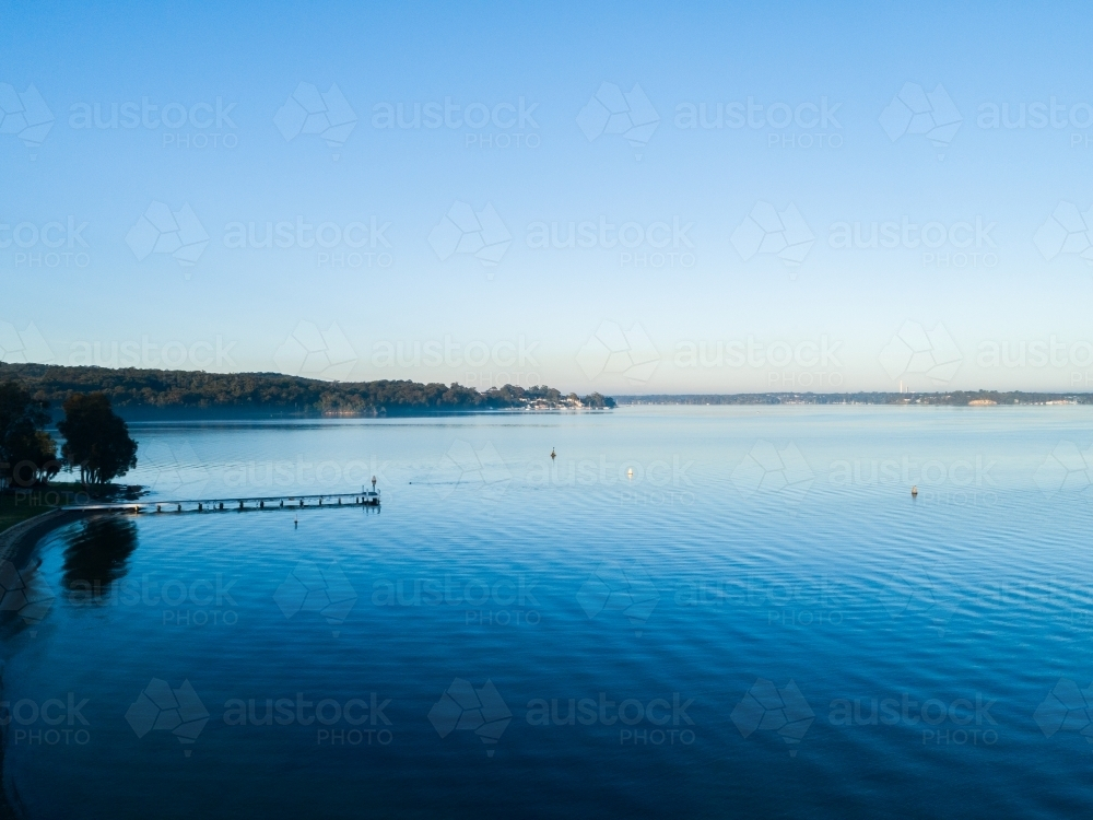 Aerial view of jetty in blue water of lake under clear morning sky - Australian Stock Image