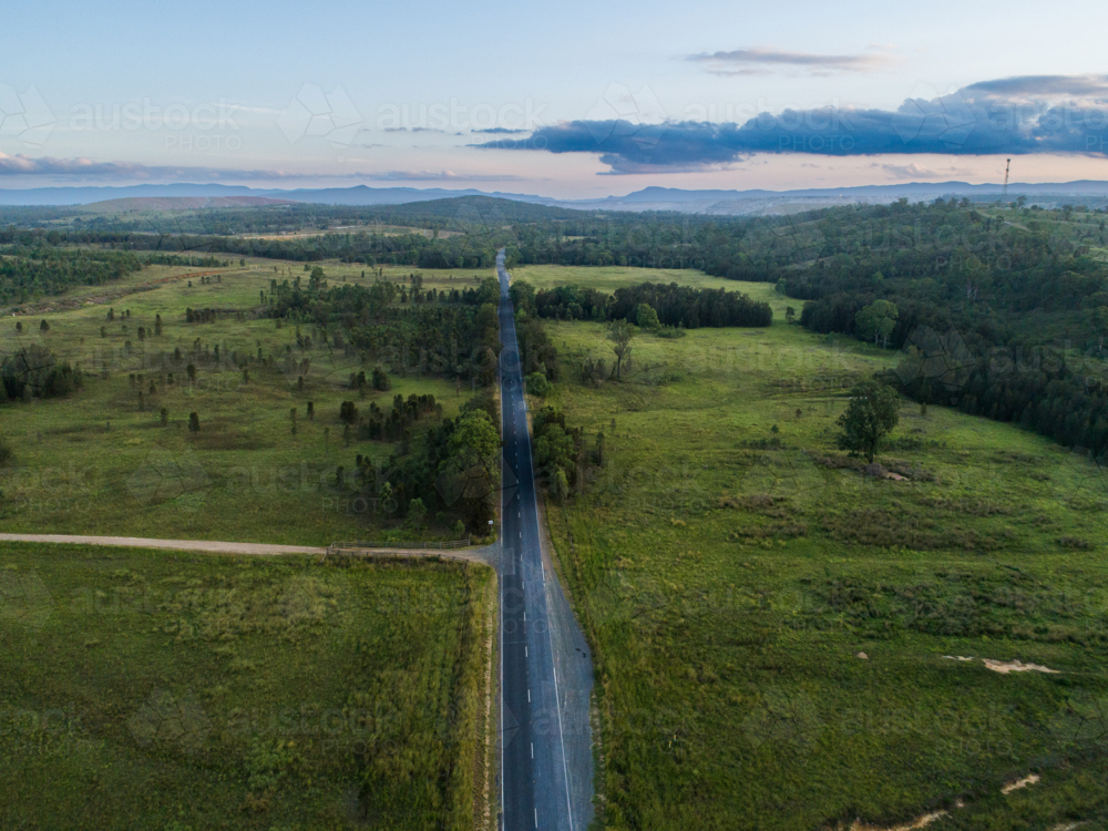 Aerial view of landscape at dusk straight country road through green paddocks with driveway - Australian Stock Image
