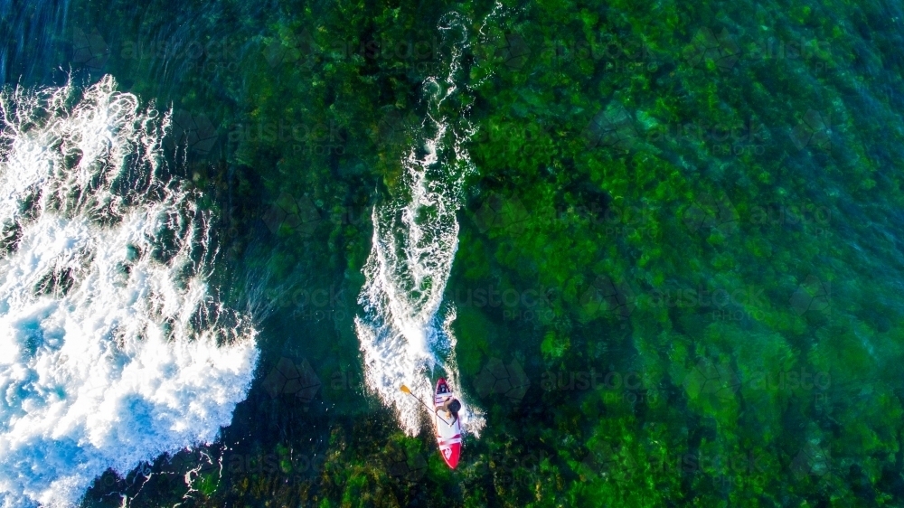 Aerial view of man riding a SUP standup paddle board at Sandon Point - Australian Stock Image